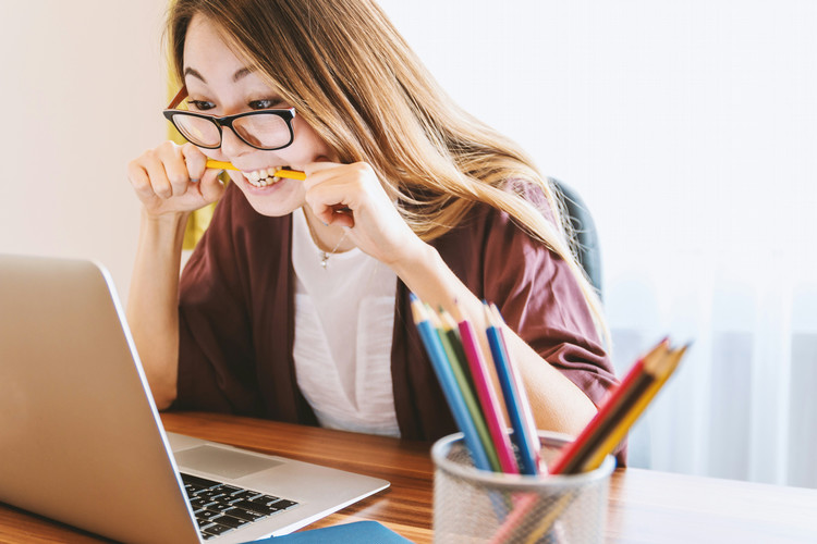 person seated in front of laptop computer and anxiously biting a pencil